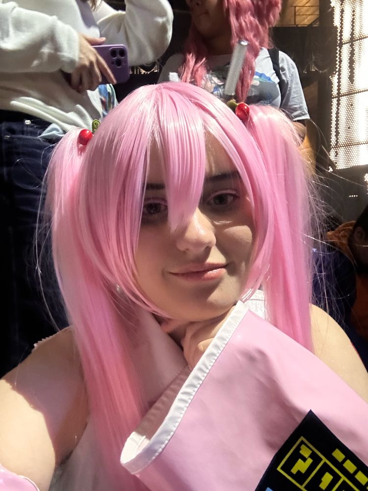 Sakura miku cosplayer sitting with hand under chin