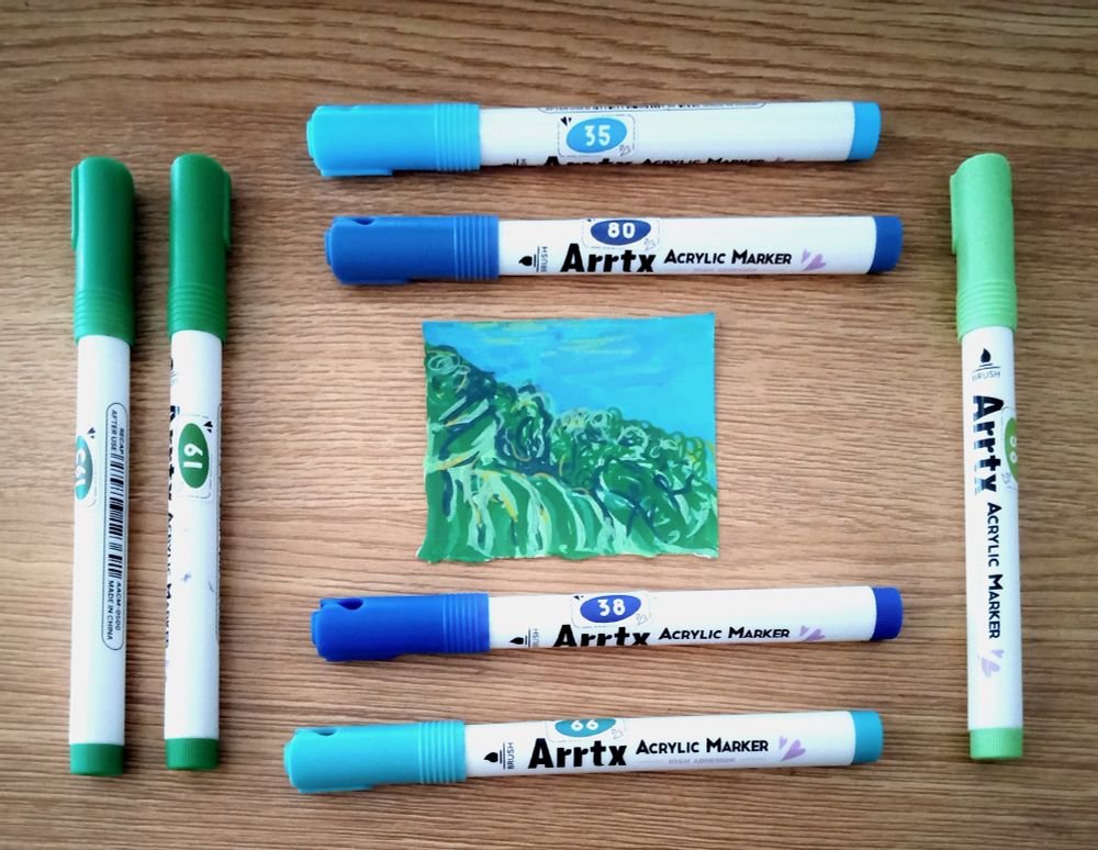 Picture of a small drawing of a field of seaweed under the sea drawn with a set of blues and greens Arrtx markers arranged around the small drawing