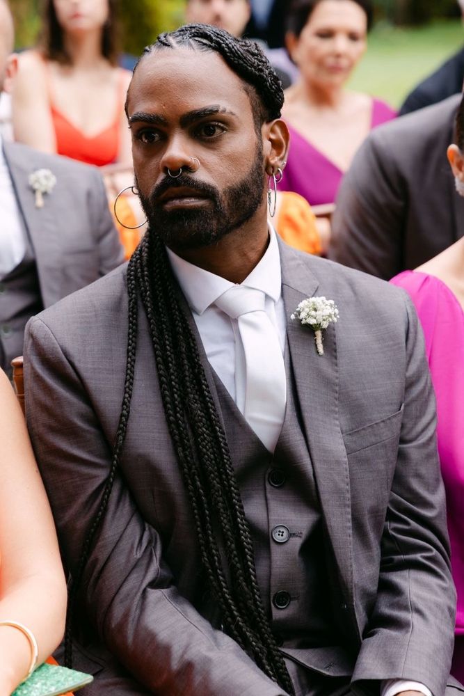 foto minha em um casamento onde estou com o cabelo com tranças nagô desenhadas e cumpridas e uso terno cinza e gravata clara.