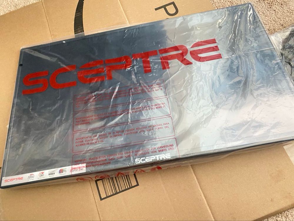 A photo of a brand new computer monitor sitting on top of a cardboard box, still in plastic wrap