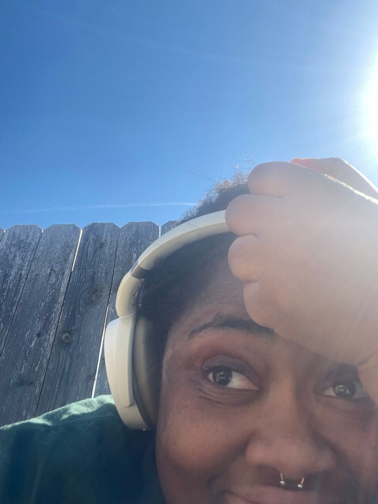 A black woman in headphones scrunched up in fearful anticipation at what this author is going to hit them with next.