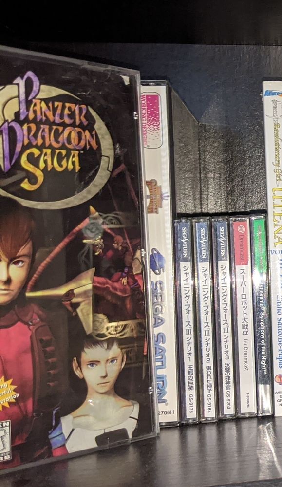 A bookshelf displaying the US releases of Panzer Dragoon Saga and Magic Knight Rayearth for Sega Saturn, and the Japanese releases of the three Shining Force III games