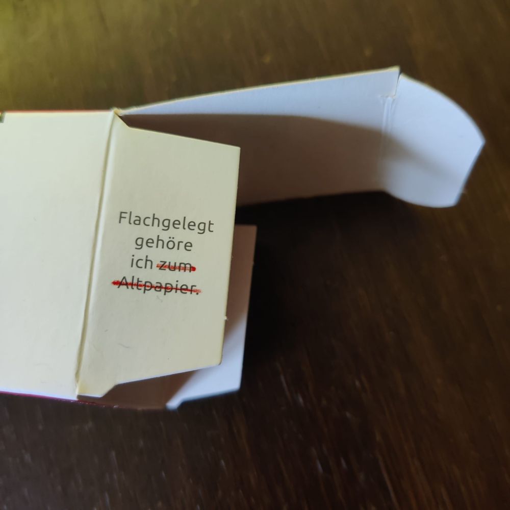 Eine Verpackungsschachtel aus Pappe mit der Aufschrift "Flachgelegt gehöre ich zum Altpapier." 
"zum Altpapier" wurde mit rotem Filzstift durchgestrichen. 