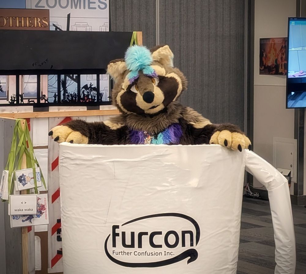 Satchel in fursuit, sitting inside a giant plush coffee mug prop with the Further Confusion logo on it. His upper torso is visible, with his arms propped up on the edges like he's sitting in a hot tub.