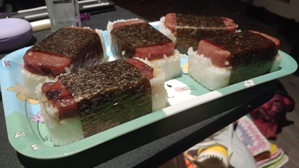 Spam musubi on my table, ready to enjoy.

Also, some background chaos lmao
