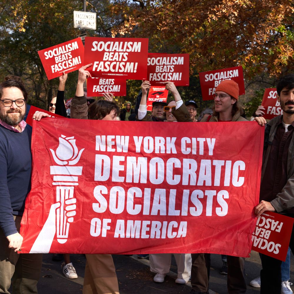 Group of people at a protest holding signs reading “socialism beats fascism! Along with a dsa flag. 