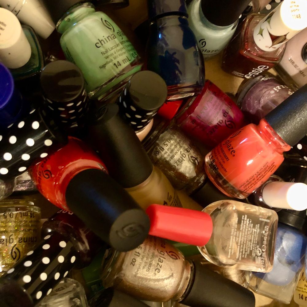 a pile of various colors of nail polish: bright red, silver, gold glitter, mint green, light blue, dark blue, purple glitter, maroon, and more