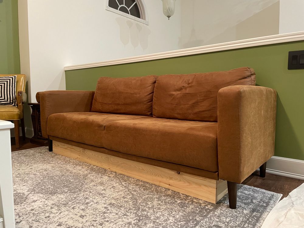 A photo of a brown couch with a plywood box talking up the space underneath