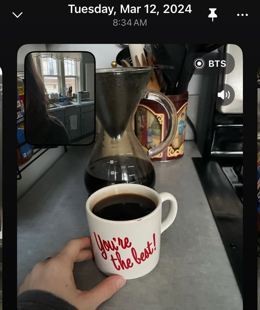 A screenshot of my BeReal post from March 12, 2024 of my hand reaching for a coffee mug, with that same cookie canister in the background (except I used it to hold cooking utensils)