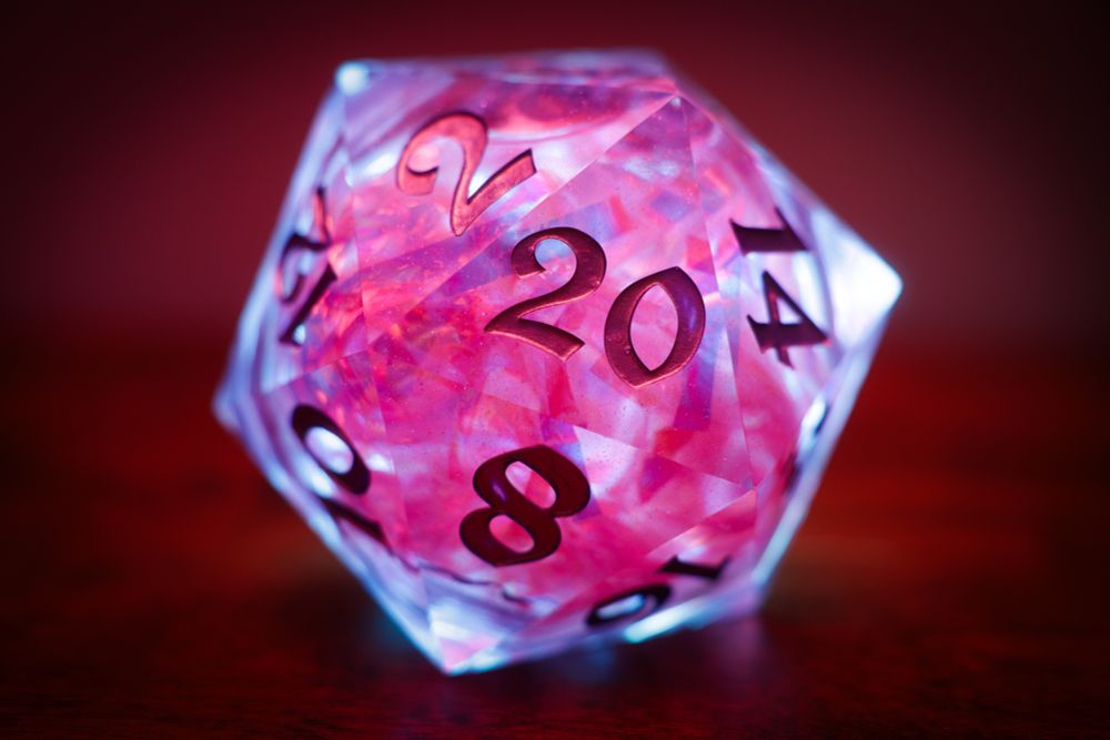 A full, centered shot of a translucent, glittery, 20-sided die (d20) resting on a dark, reddish-brown surface. The die is glowing with a vibrant red and pink light from within, making the number 20 and the surrounding numbers (like 8, 2, 14) clearly visible in a dark font.