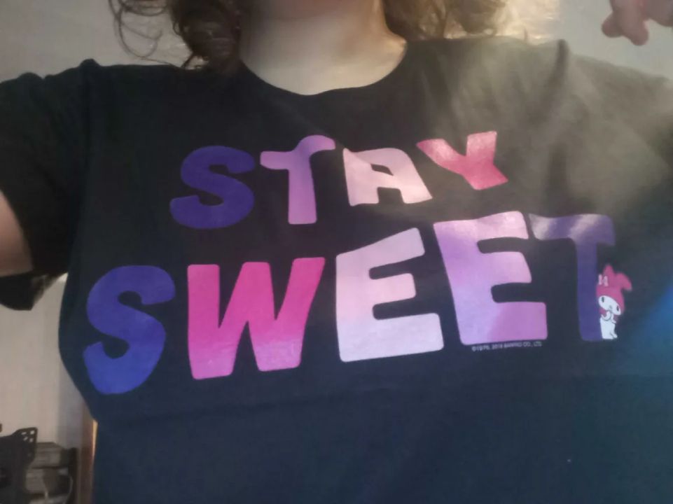 STAY SWEET - black shirt with colored STAY SWEET text on it, accompanied by Sanrio character My Melody standing by the last T