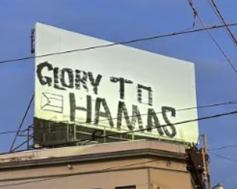 Photo caption: The pro-Hamas graffiti has been widely condemned by political leaders and members of the Jewish community. (ABC News)

The photo shows a rooftop billboard with "Glory to Hamas" printed in large black all-caps against a white background.

The lettering is uneven, suggesting a rushed, hurried scrawl. 

The Palestinian flag outline is positioned between "GLORY TO" and "HAMAS," rendered as a simple black line drawing (not filled with the traditional colours of black, white, green, and red). This monochromatic outline blends somewhat into the shadows and text, making it less prominent than a full-colour version might be.