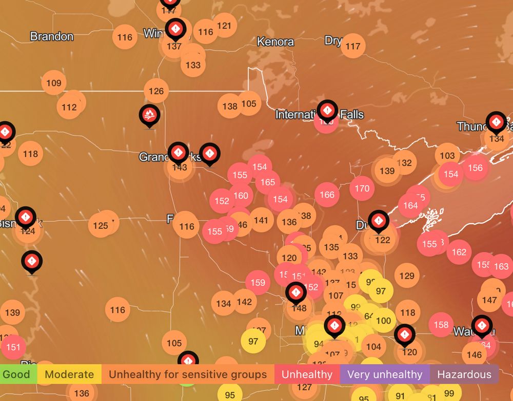 An Air Quality Index (AQI) map showing the Upper Midwest United States (centered around Minnesota) and south-central Canada. The map is filled with colored circles containing numbers, which represent the AQI for various locations. A color-coded legend at the bottom shows the scale: green for "Good," yellow for "Moderate," orange for "Unhealthy for sensitive groups," red for "Unhealthy," purple for "Very Unhealthy," and dark purple for "Hazardous." Many of the visible areas, particularly in the center of the map, are colored red, with AQI values often exceeding 150, indicating poor air quality resulting from wildfires ravaging forests in Canada.