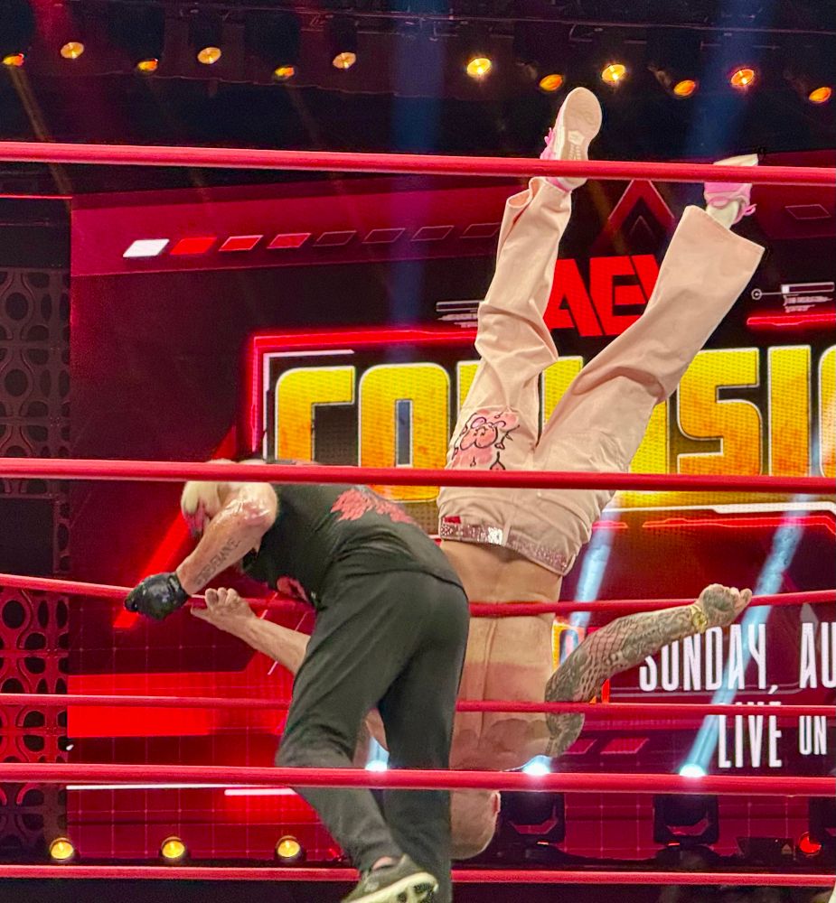 Dustin Rhodes dumping Kyle Fletcher over the ring ropes onto the floor. Kyle’s legs are sticking straight up.