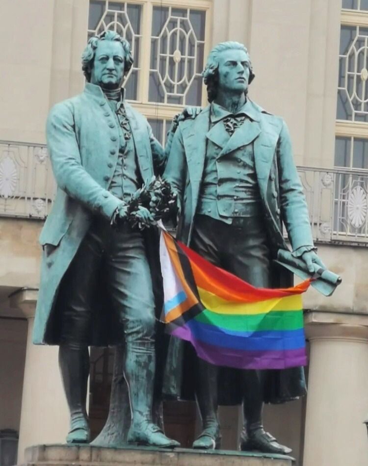a statue of Goethe and Schiller holding a pride flag