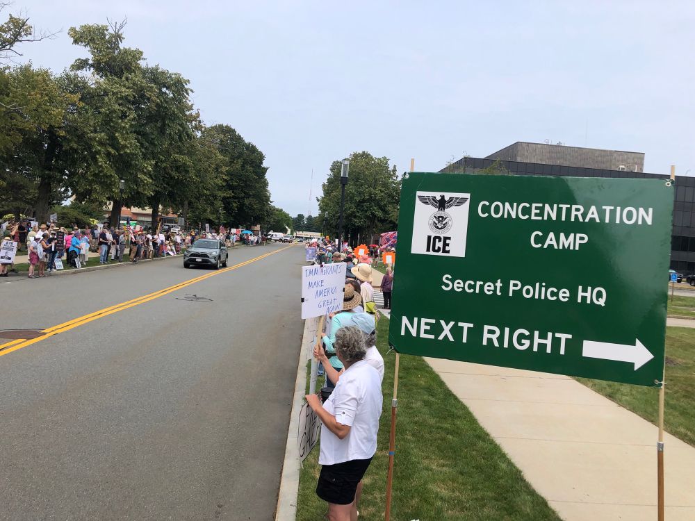 Hundreds of peaceful protesters at ICE Burlington MA with a sign in the foreground that says “ICE Concentration Camp” Next Right
