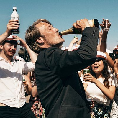 Fotograma de la película 'Otra ronda'. El protagonista bebe de una botella de champagne en plena calle, vestido de negro, mientras que una multitud también celebra con él, todos con alcohol en la mano en botellas y latas.