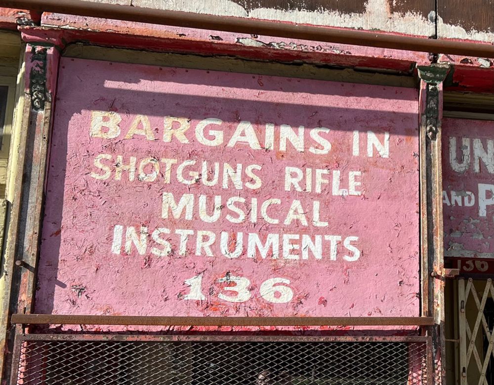 Sign reading “Bargains in Shotguns, Rifle, Musical Instruments”