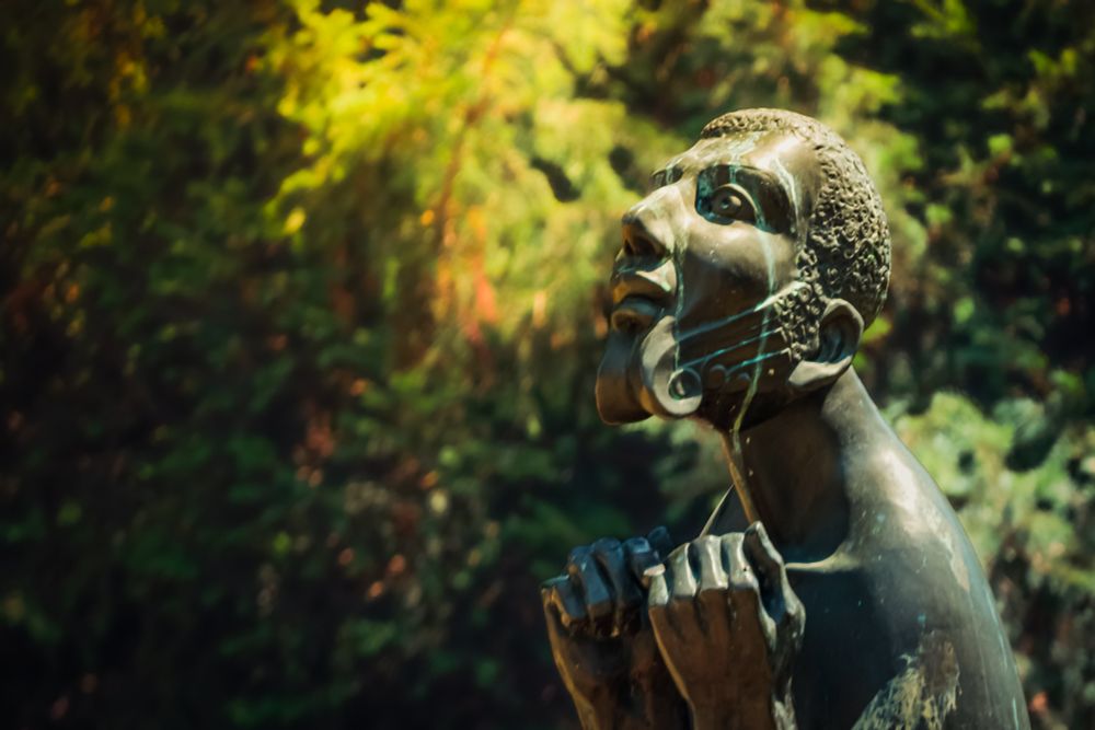 A bronze statue with it's face to the sky, hands raised to chest height.