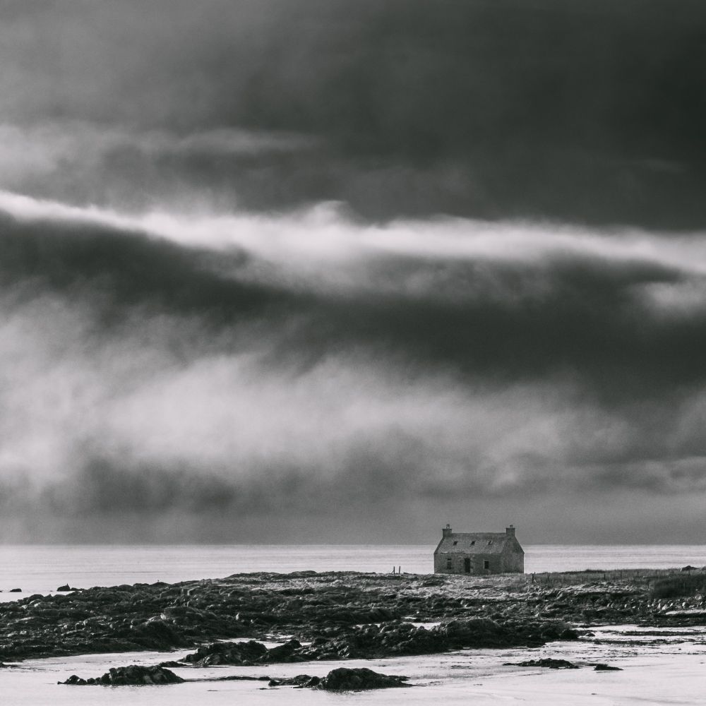 An abandoned croft house in front of a bank of fog.