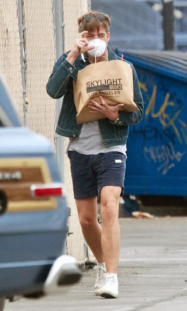 Chris Pine wearing a Covid-era mask, in shorts and a jacket, carrying a large bag with Skylight Books Los Angeles printed on it