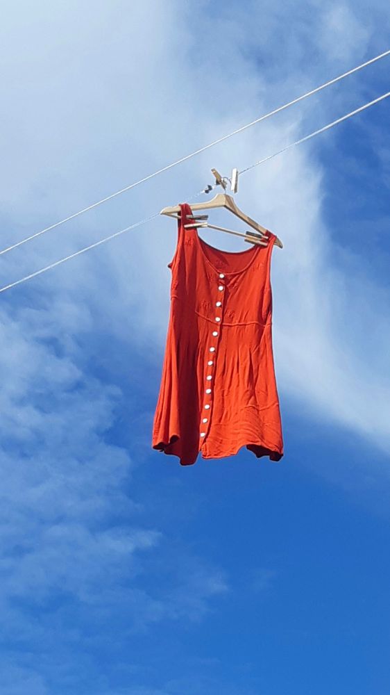 Red orange dress hanging on the clothes line below blue sky and soft cloud
