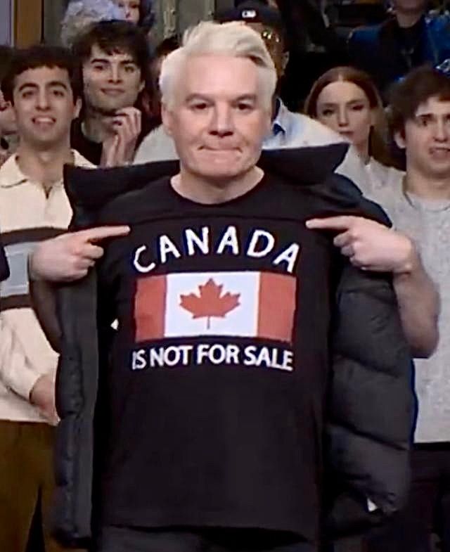 Mike Myers points to the shirt he’s wearing on SNL that says Canada is not for sale. 