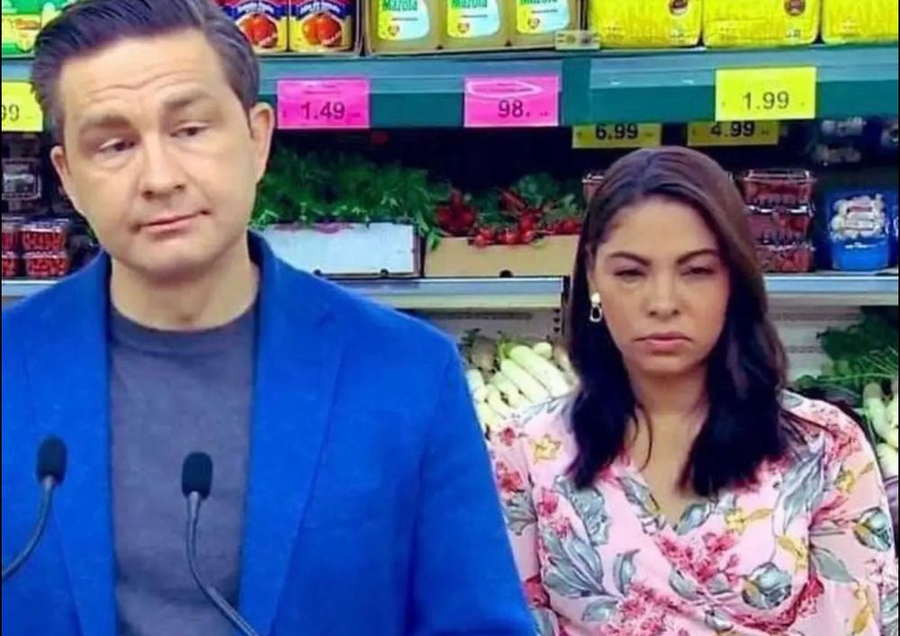 Anaida Poilievre scowls beside her husband Pierre while he gives a press conference in the produce section of a grocery store. 