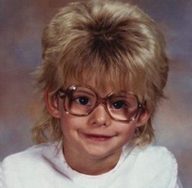 A child with an enormous blonde mop of hair and awkward glasses. 