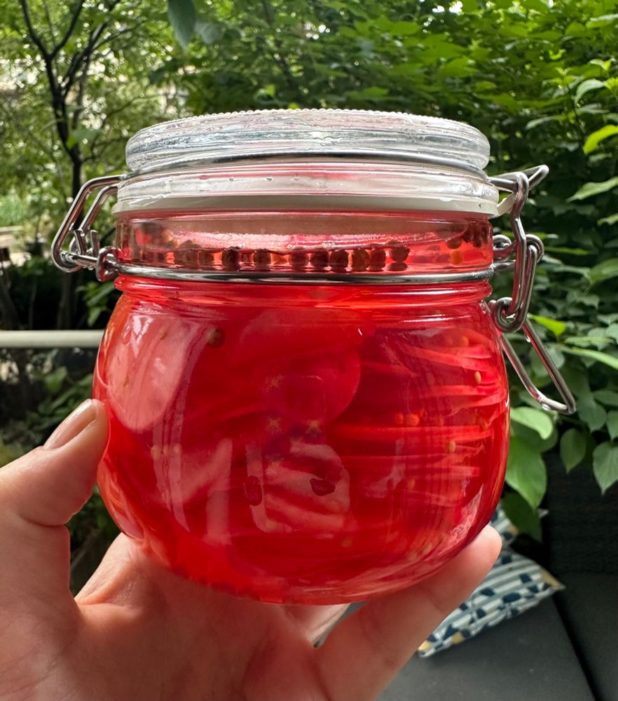 A hand holds an IKEA storage jar filled with ruby red deliciousness in the form of quick-pickled radishes. 