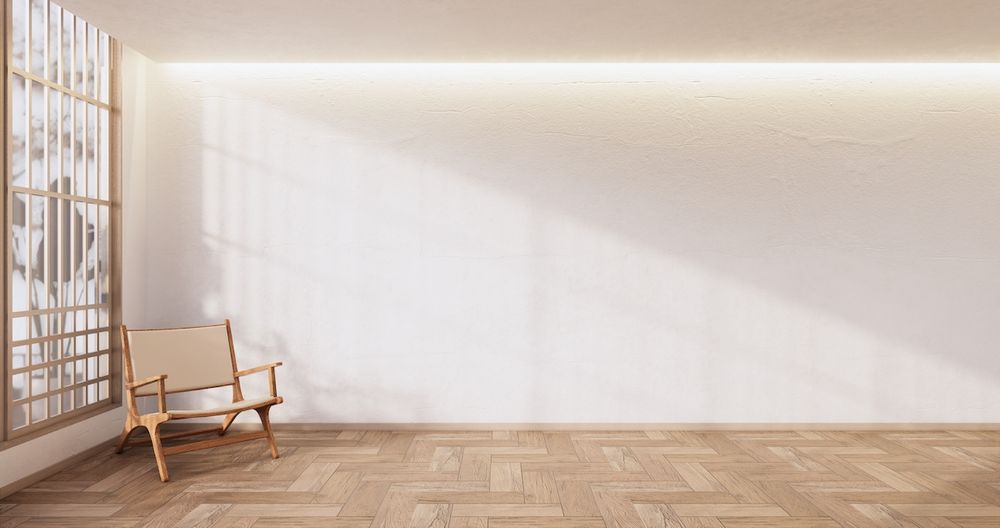 A room with white walls, a wood floor, and a single, minimalist armchair in the corner.