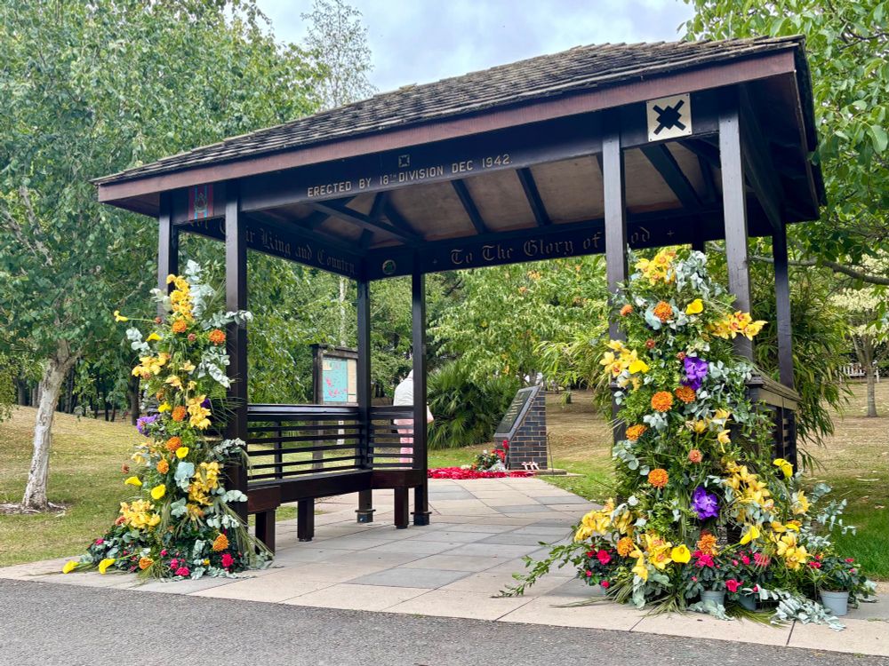 A wooden lych gate - originally built at Changhi Prsion and now installed at the National Memorial Arboretum - is dressed with flowers. 