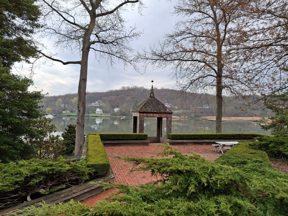 Picture of a wide patio leading to a gazebo overlooking a harbor with houses and trees on the other side of water.