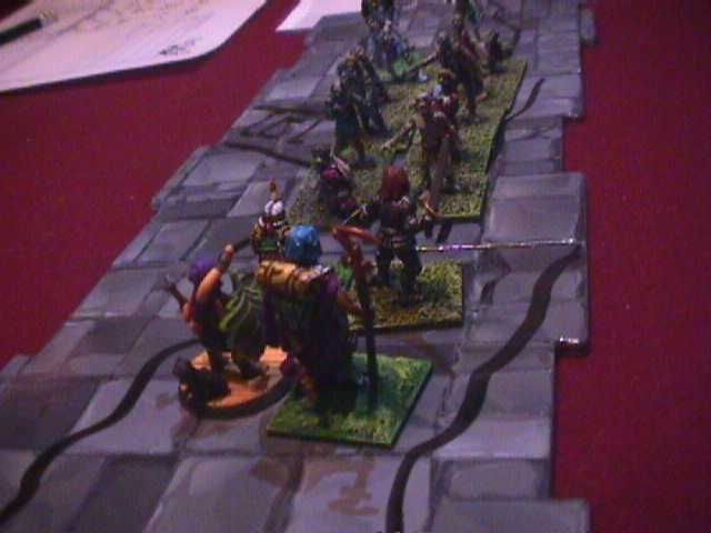 On a red felt table sits dungeon tiles made of card. A collection of scale models of adventurers and monsters sit on the tiles, engaged in combat. The photo is a low resolution.