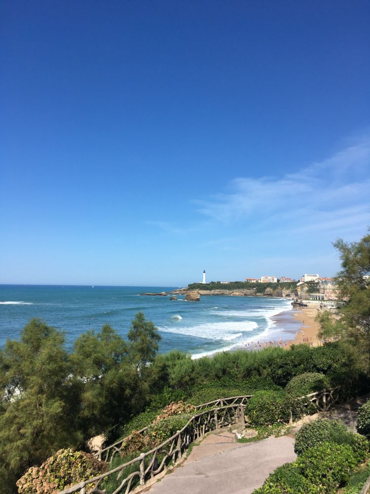 Photo of the beach from Biarritz, sunny with a clear blue sky showing a lighthouse in the distance
