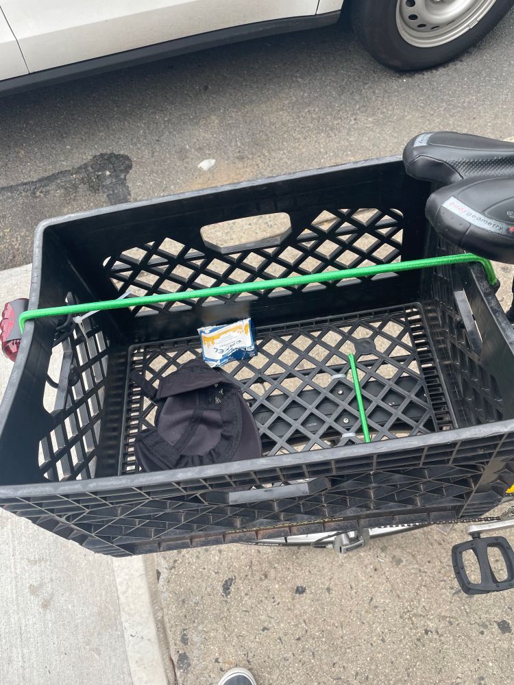 milk crate on a bicycle with a discarded hat and cigarette pack in it