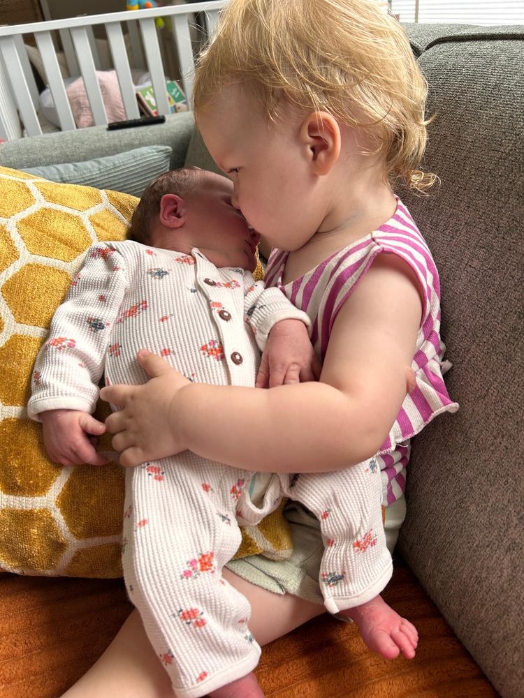Grote zus van 2 met kleine zus van 2 weken op schoot waarbij zij haar heel lief kust