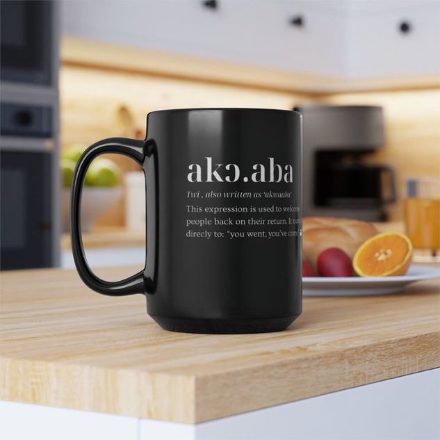 Closeup of a mug sitting on a chopboard, in a well-lit kitchen, that has the Twi word for welcome, “Akoaba”, designed on it.