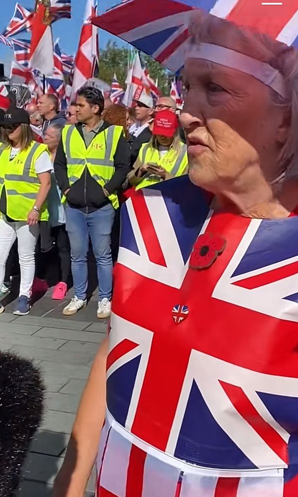 an old woman with a union flag hat, a union flat shirt with a poppy and union flag badge on and a skirt made of the st george’s flag