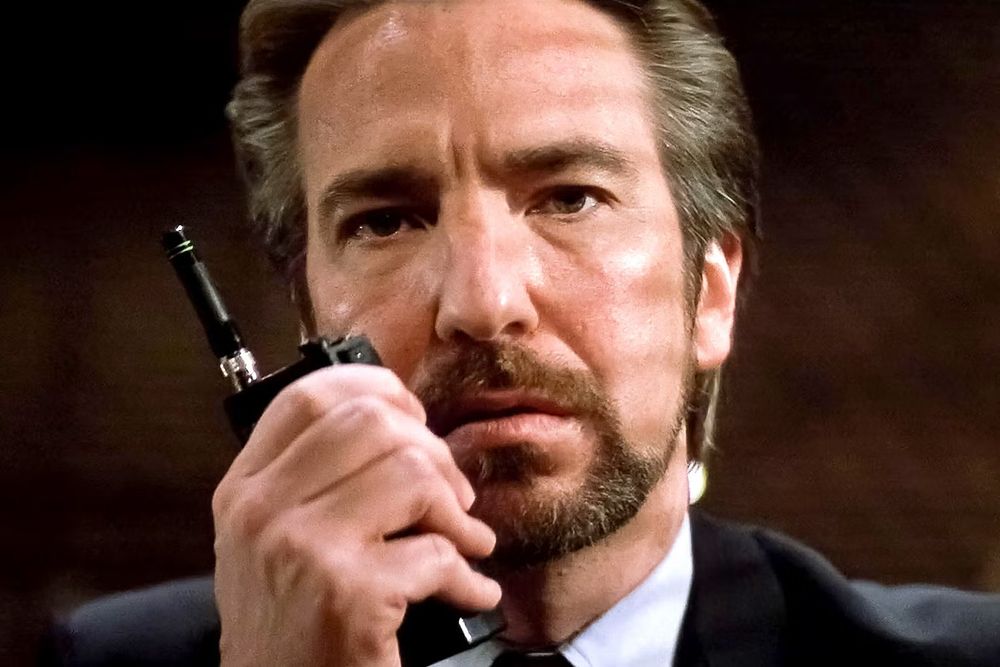 a man in a suit with a beard holding a walkie talkie to his face. 