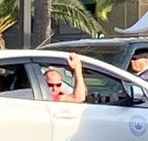 man in sunglasses with his arm out the passenger side car window is getting an eyeful of Hawkwoman.  A day he'll never forget.