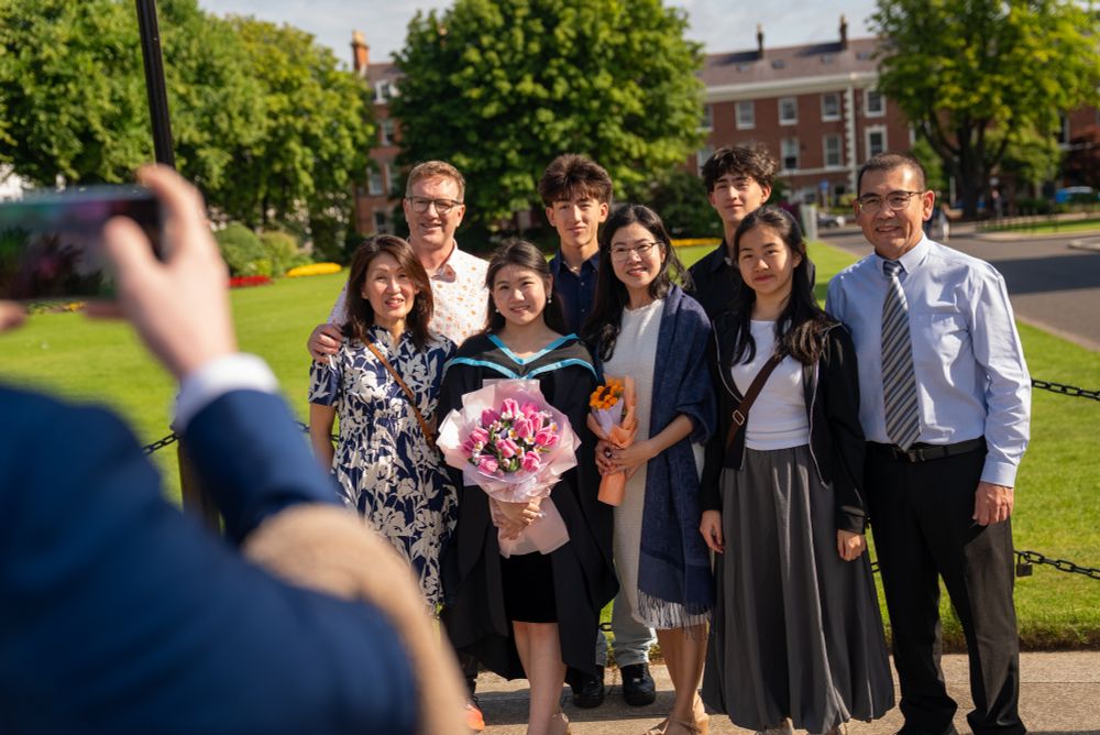 Image shows a family having their picture taken at graduation. The image is taken from behind the camera.