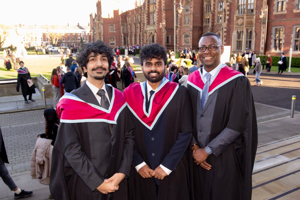 Image shows Mohammed Suffiyan Rasheed from Pakistan, Suyash Shrishail Mhamae from India and Daniel Pelu from Ghana celebrating as they graduate with Master’s in International Relations. They are pictured in front of the Lanyon Building.