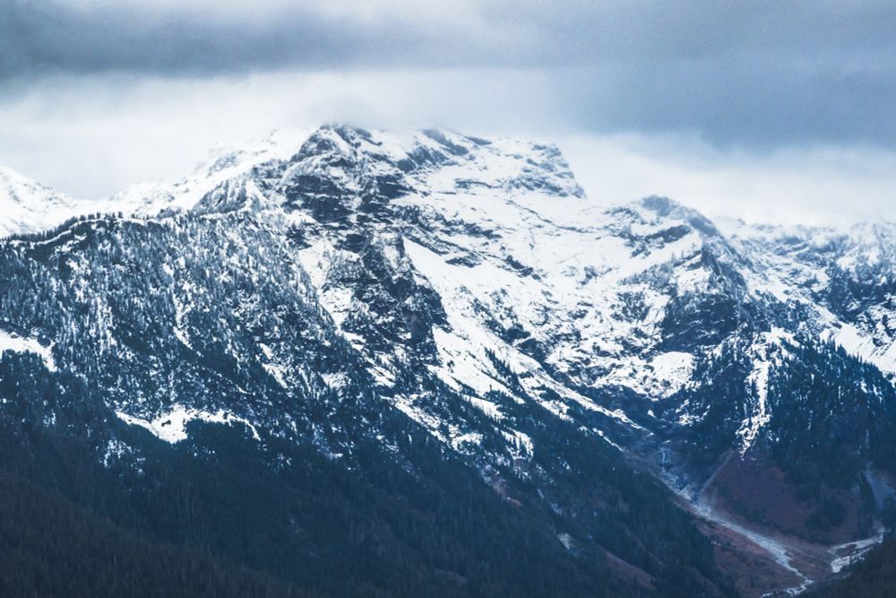 Kyes Peak stands tall with a mix of snow and exposed rock, surrounded by steep forested ridges and a narrow valley below. Captured from Frog Mountain in the Henry M. Jackson Wilderness, Washington.