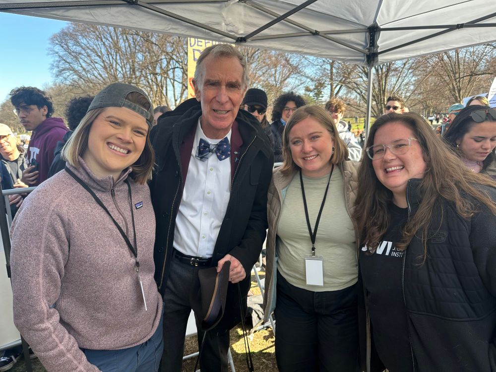 3 women pose with Bill Nye. 