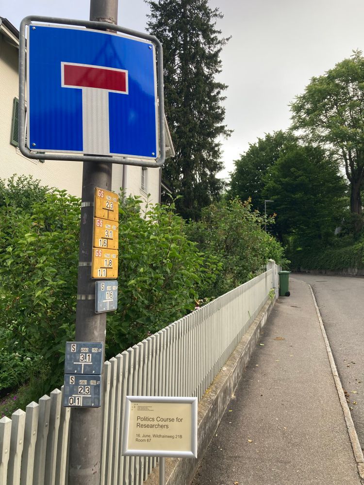Photo of a narrow street with a big dead end sign and, below it, a sign reading "Politics Course for Researchers"