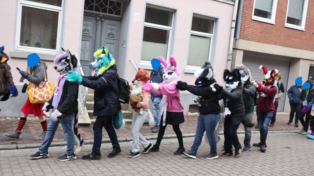 Some furries walking with their hands or paws on each other shoulders of the furry in front