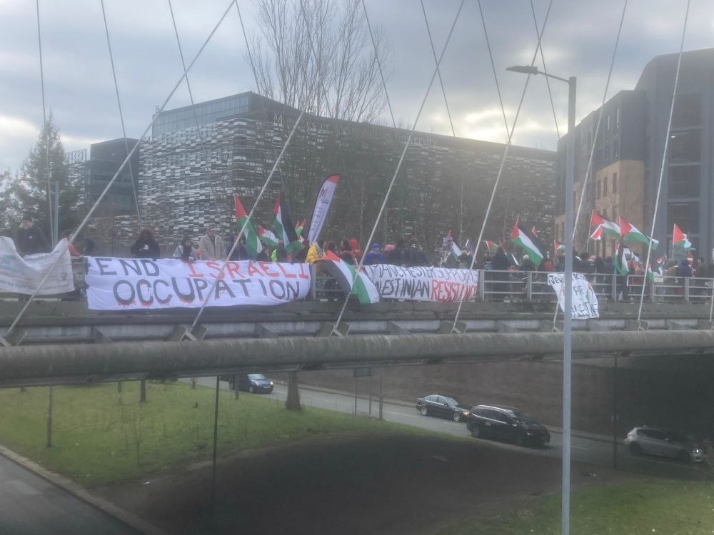 A banner drop on Hulme arch in Manchester. Visible are banners reading “end Israeli occupation” and “Manchester supports Palestinian resistance” and many people waving Palestinian flags