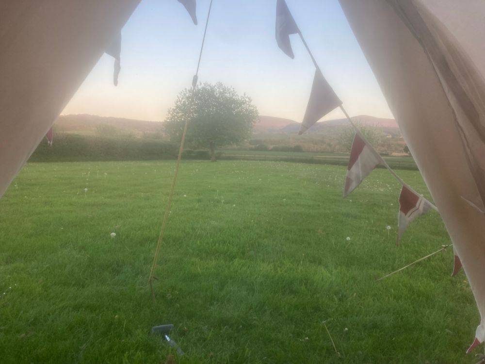 A view out of a tent of a green field with hills behind