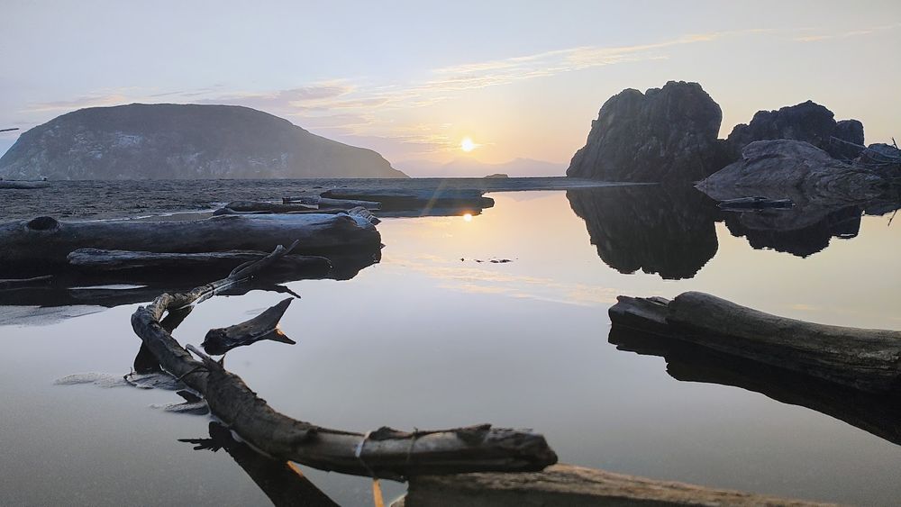 Sunset at Harris Beach State Park, Oregon coast. Foreground is driftwood in a tide pool. Background besides the sun are a few small islands/sea stacks.